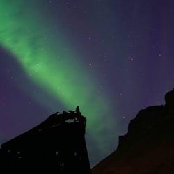 With the rusty boat and cliff silhouetted, the aurora is a shot across the bow. *