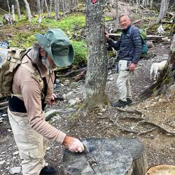 Manuel schlägt auf der Tischplatte mit einem Stein einen herausstehenden Nagel ein.
