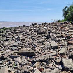 Boulder and building rubble strewn beach looking south