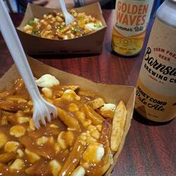 Die berühmten Poutine - Pommes mit Gravy (veg. Bratensoße) und Käse. Serviert mit lokalem Bier.