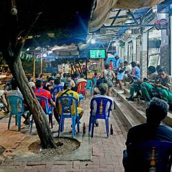 Einheimische schauen sich das Spiel vor den kleinen Läden an