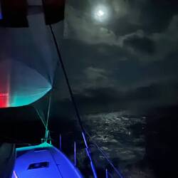 Die Postionslichter (rechts/ links) spiegeln sich im Segel, der zunehmende Mond im Wasser