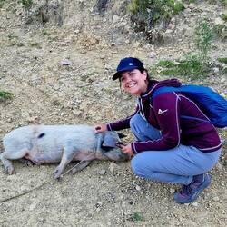 Hanna streichelt ein angebundenes Schweinchen, das sich sogleich hinlegt und geniesst.