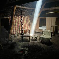 The only light in the 1700s house is focused in the smoke from the fire