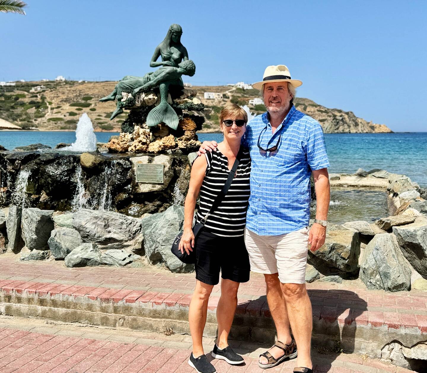 In the village of Kini in front of a statue of a mermaid holding a fisherman.