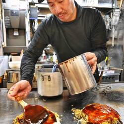 Typisch Hiroshima: Okonomiyaki (Haufen aus Pfannkuchen, Kohl, Sprossen, Nudeln, Ei, Spezialsoße.