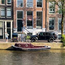 Electric boat, and two electric cars in front of canal homes.