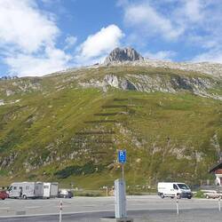 Großer Parkplatz auf dem Oberalppass. Im Hintergrund fährt eine Gondelbahn auf den Gipfel.