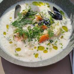 Fischsuppe gerahmt mit Fisch, Muscheln, Garnelen und Dillöl