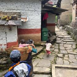 A grandmother carrying her granddaughter in a basket w strap around her forehead