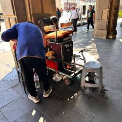 Man thront buchstäblich bei den Schuhputzern - hartes Leben heute, auch er trägt Sneakers