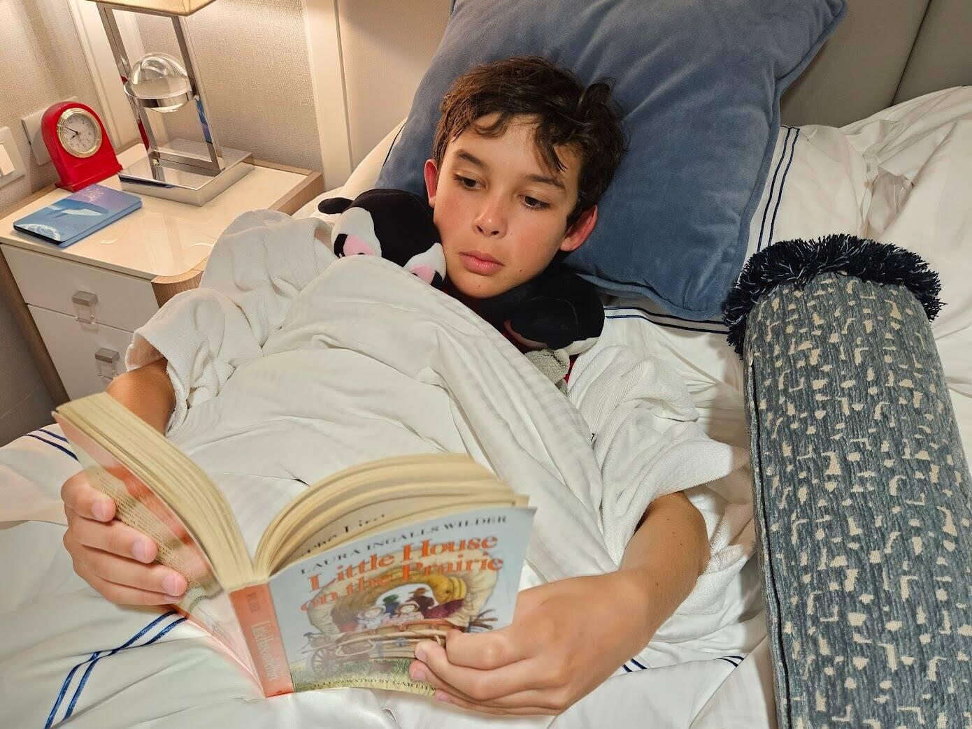 DJ reading his assigned book with his penguin neck pillow from Simon's Town