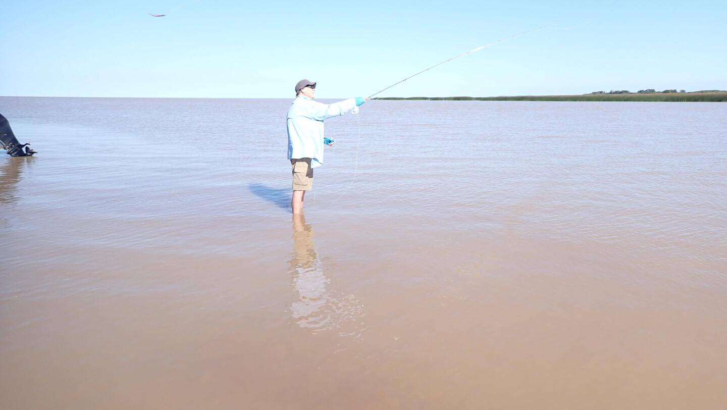 Some old guy with skinny legs fly fishing in the mud