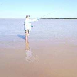 Some old guy with skinny legs fly fishing in the mud