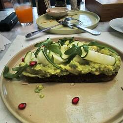 Grob pürierte Avocado, hauchdünne, rohe Zucchini auf einer dicken Scheibe Sauerteigbrot