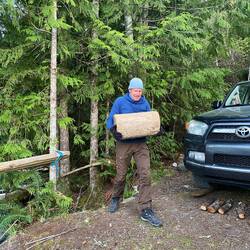 Aron hievt schwere Treibholzstämme zum Sitzen am Lagerfeuer hoch.