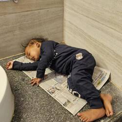 Das Kind einer Toilettenfrau schläft neben einem Waschbecken...