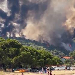 Urlauber baden – hinter ihnen brennt der Wald
