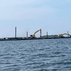 Tug pushing two barges with some big backhoes on them.