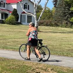 Rosanne walking her bike up the gravel driveway (hill) to the Fort Plain Museum