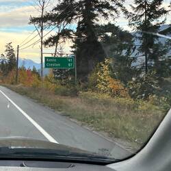 Zwischen buntem Laub und Bergpanorama zeigt das Schild die Entfernungen zu Kaslo und Creston.