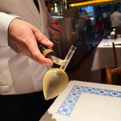 Kellner mit Krawatte und weissem Jackett. Stilvoller Glaskolben als Messbecher.