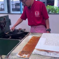 The worker presses the copper pattern block (the cap) on the stamp-pad then applies the cap on cloth