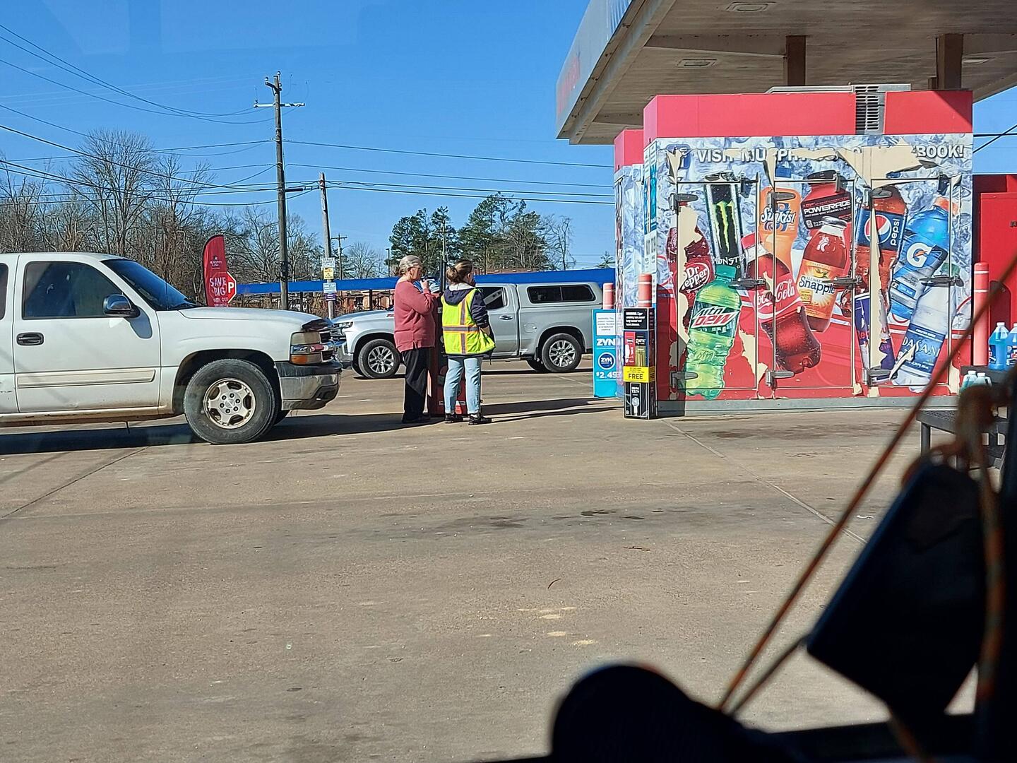 Frau Tankwart (gelbe Weste) und Kundin stehen rauchend an der Zapfsäule beim Tanken.