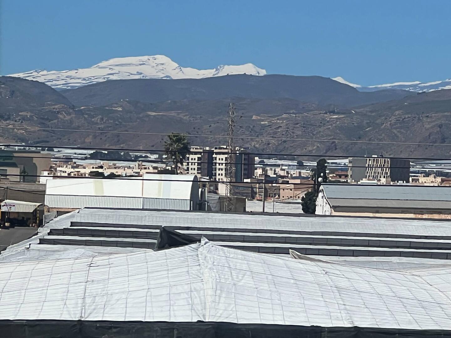 Schnee der Sierra Nevada und im Vordergund weiß von den Folien der Gewächshäuser