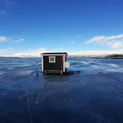 eine Seasonhütte mit Bett, Gaskocher und Angel mitten auf dem Eis