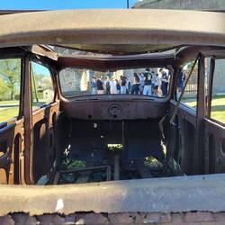 Looking through the car windows of a burnt out car wreck towards the visiting French school group