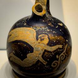 Squat Lekythos (used to dispense oils or perfume) with the figure of a winged youth; likely Eros.
