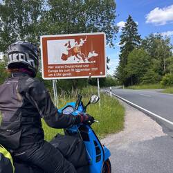 Zisi hält vor dem Schild, dass die ehemalige Innerdeutsche Grenze markiert.