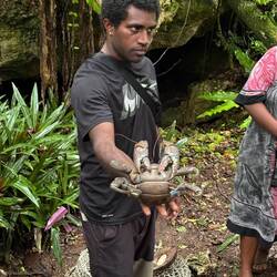 Daniel holding a coconut crab, a local staple. Grotto behind him