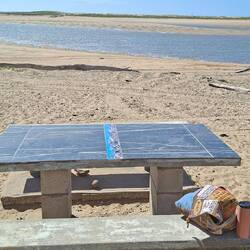 A cement table and chairs and fire pit on the beach. Obviously for the locals.