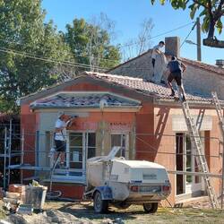 The render is applied, the labourer is cleans up the old render, and the plumber is also on the roof